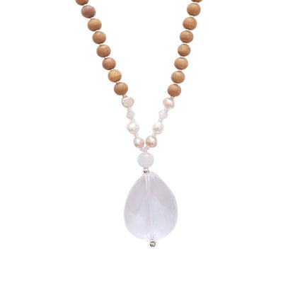 Close up image on a white background of a mala necklace. The mala has a faceted pear shaped Clear Quartz Guru Bead . Above the guru stone is a single rainbow moonstone bead. On each side above the rainbow moonstone, is one pink pearl, one white pearl, one diamond shaped peach glass bead and one more pink pearl. The rest of the mala is made with 6mm sandalwood beads separated by 2mm silver spacer beads. 