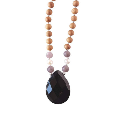 Close up image on a white background of a mala bead necklace. The mala has a pear shaped faceted onyx guru bead.   On each side above the Onyx guru is one purple lepidolite bead, one pearl and one more lepidolite bead. The rest of the mala is made with 6mm sandalwood beads separated by 2mm silver spacer beads.