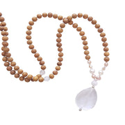 Close up image on a white background of a mala necklace. The mala has a faceted pear shaped Clear Quartz Guru Bead . Above the guru stone is a single rainbow moonstone bead. On each side above the rainbow moonstone, is one pink pearl, one white pearl, one diamond shaped peach glass bead and one more pink pearl. The rest of the mala is made with 6mm sandalwood beads separated by 2mm silver spacer beads. In the middle of the necklace is a single clear quartz bead on each side.