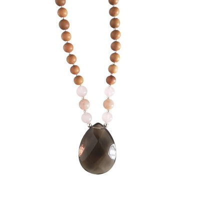 Close up image on a white background of a mala necklace with a teardrop shaped Smoky Quartz  guru bead. Above the guru bead are rose quartz and light pink moonstone beads followed by 6mm sandalwood beads separated by 2mm silver beads.