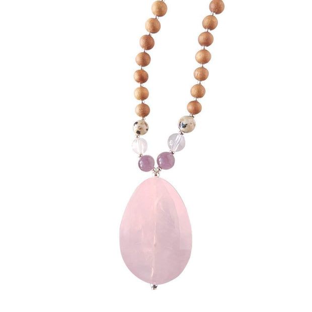 Close up image on a white background of a mala necklace with a teardrop shaped Rose Quartz guru bead. Above the guru bead are lepidolite, dalmation jasper and clear quartz beads followed by 6mm sandalwood beads separated by 2mm silver beads.