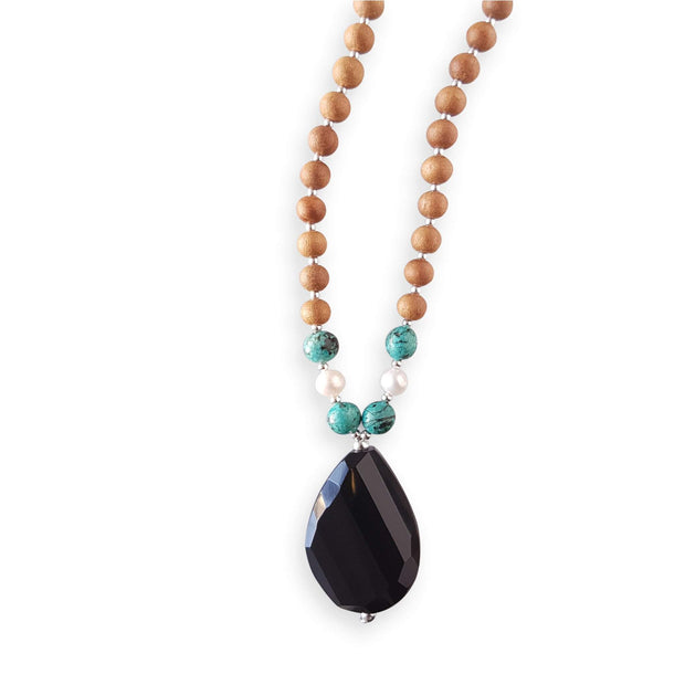 Close up image on a white background of a mala necklace with a teardrop shaped Black Onyx guru bead . Above the guru bead are pearl and turquoise jasper beads followed by 6mm sandalwood beads separated by 2mm silver beads.