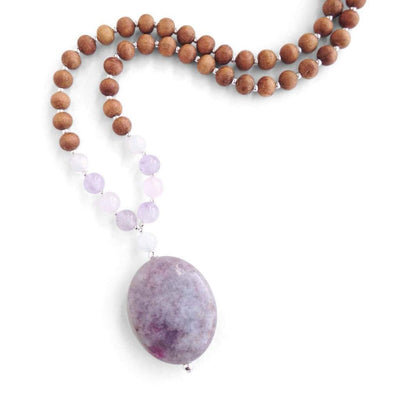 Close up image on a white background of a mala necklace with an oval shaped Lepidolite guru bead . Above the guru bead are moonstone, amethyst and rainbow moonstone beads followed by 6mm sandalwood beads separated by 2mm silver beads.