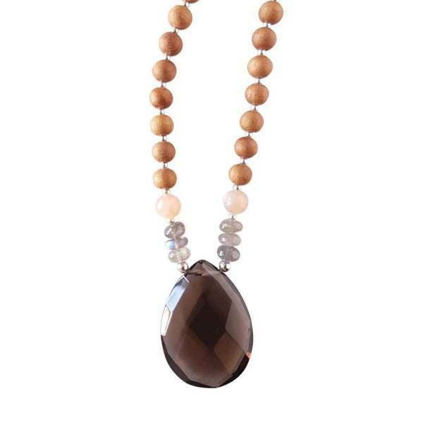 Close up image on a white background of a mala necklace with a pear shaped Smoky Quartz guru bead . Above the guru bead are pink moonstone and labradorite beads followed by 6mm sandalwood beads separated by 2mm silver beads.